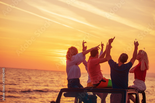 Five young people having fun in convertible car at the beach at sunset.