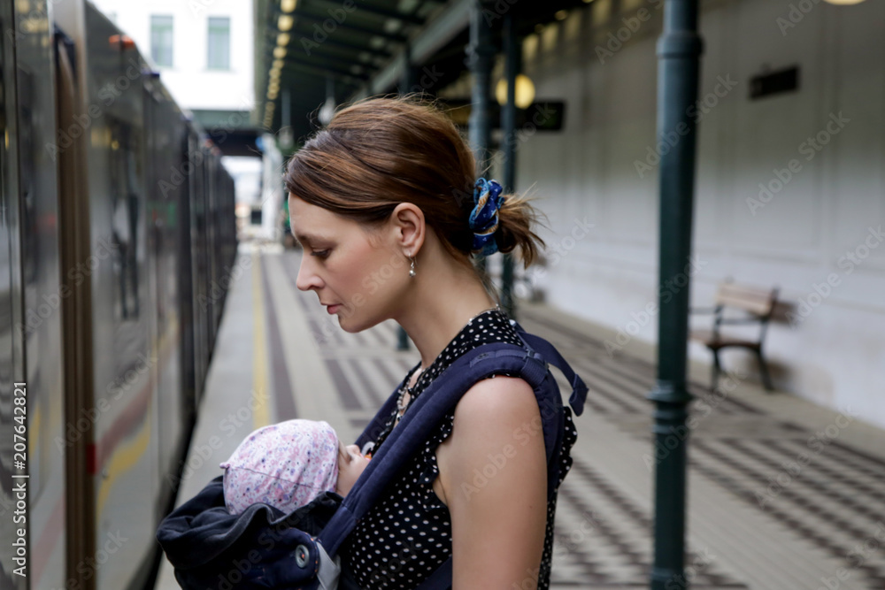 Young mother with infant baby in carrier waiting for metro on the station