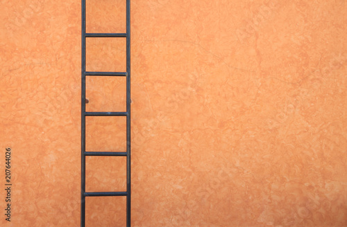 Iron ladder on painted cement wall.