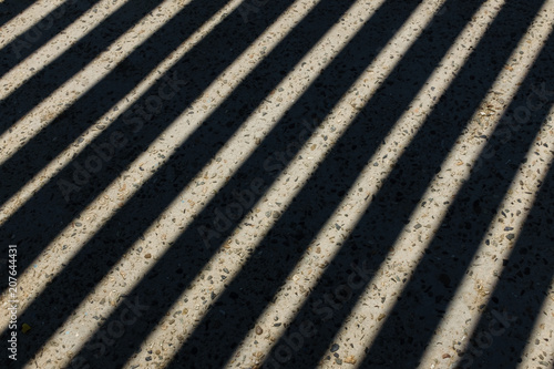 Sunlight shines through wooden fence and makes geometric stripes shadows on the ground. Shadows of wooden fence on the ground. Fence shadows texture