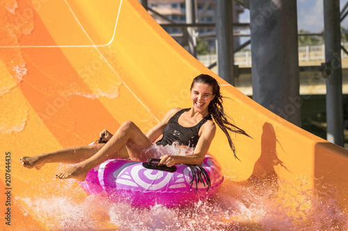 pretty woman on the rubber ring having fun on the orange water slide in the aqua park. Summer Vacation. Weekend on resort