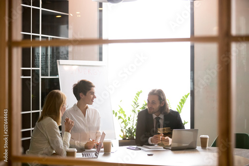 3 smiling business colleagues having casual conversation in boardroom, businessman talking, sharing thoughts with businesswomen, discussing contract in friendly office atmosphere. Cooperation concept