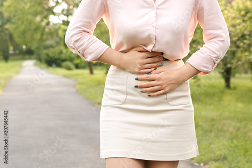 Young woman suffering from abdominal pain while walking in park.