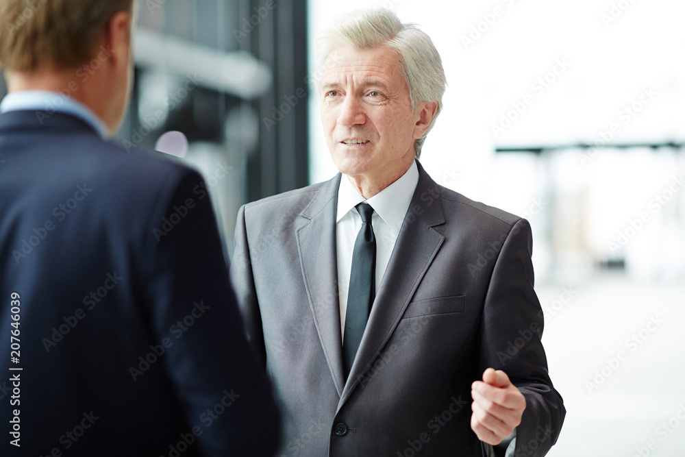 Mature businessman in formalwear discussing forthcoming conference or other event with foreign colleague in airport