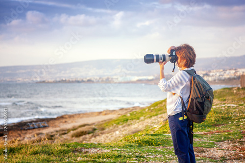 Young girl professional photographer on the beach with a camera in hand, travel and remote work, blogger