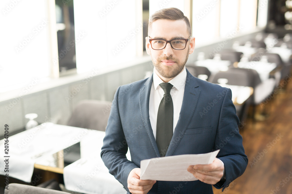 Confident agent or banker in suit and eyeglasses lookig at you while working with financial papers