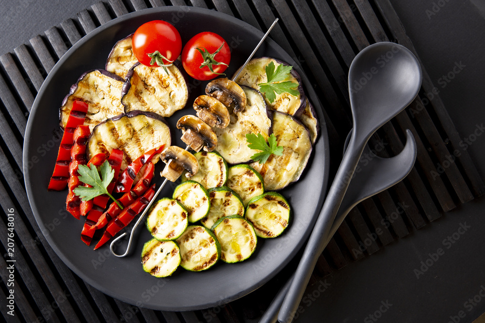 Grilled vegetables: eggplant, zucchini, pepper. Skewer with mushrooms. On a black plate and a black background. Toned. Grilled vegetables: eggplant, zucchini, pepper. Skewer with mushrooms. On a black plate and a black background. Toned.