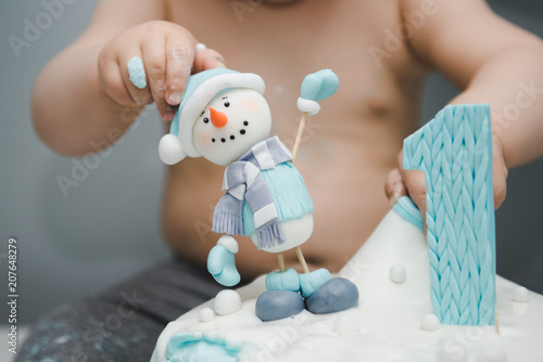 Cute little boy eating his first birthday cake. Baby cake smash. Birthday cake for 1 year old boy. Winter cake with a snowman.