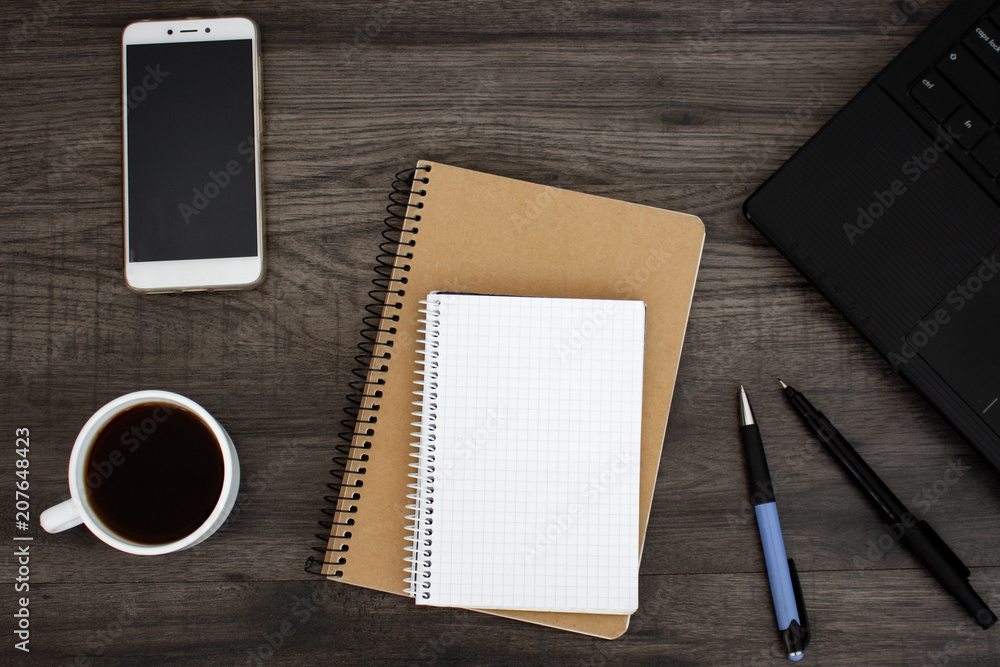 Open blank notepad, pens, coffee, phone and laptop on the dark wooden table. Workplace flat lay Open blank notepad, pens, coffee, phone and laptop on the dark wooden table. Workplace flat lay