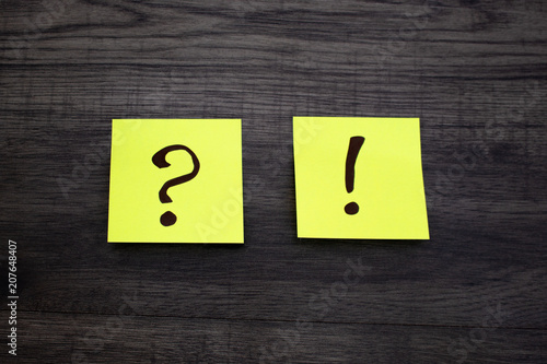 Question mark and exclamation point on a yellow sticker on a dark wooden background