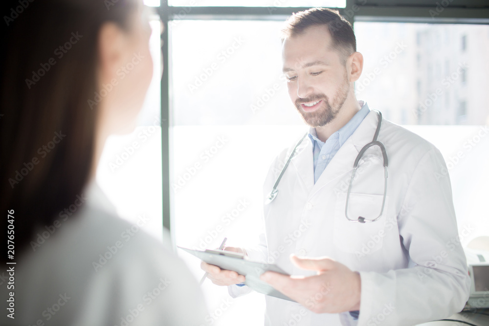 Happy young doctor reading medical notes while communicating with his colleague or assistant Happy young doctor reading medical notes while communicating with his colleague or assistant