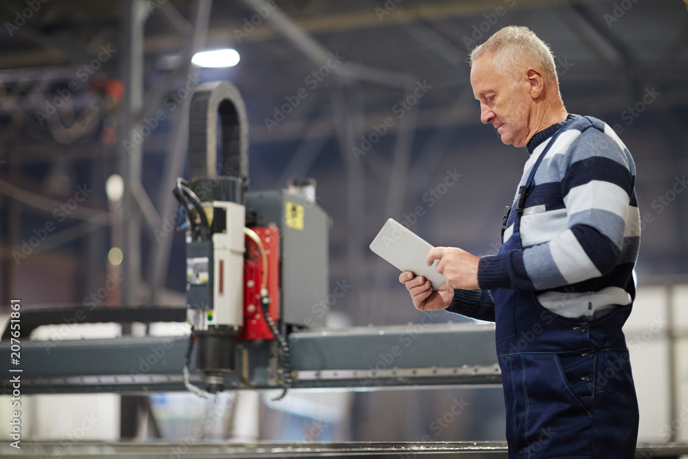 Serious mature worker with touchpad searching for online information while working in shipyard Serious mature worker with touchpad searching for online information while working in shipyard