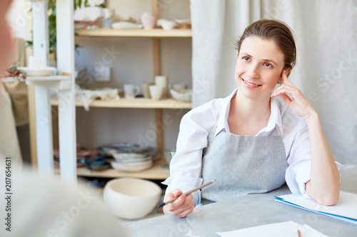 Friendly young female talking to her client about details of order in workshop