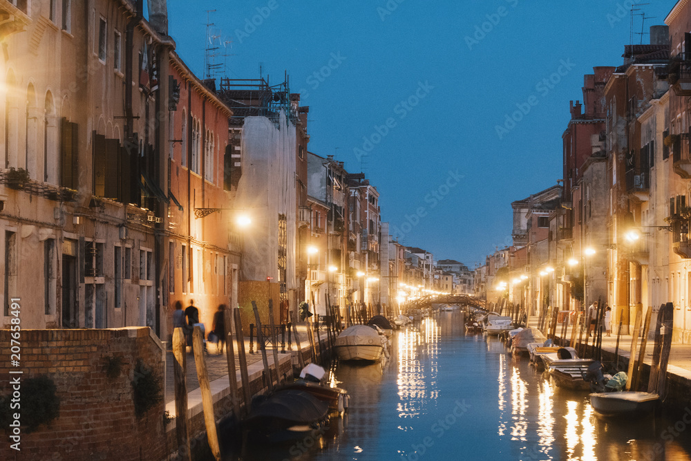 Water canal and colorful historic houses at night in Venice, Italy