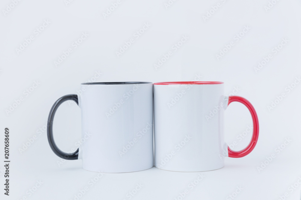 Two white mugs, with a black and red handle on a light background. Two white mugs, with a black and red handle on a light background.