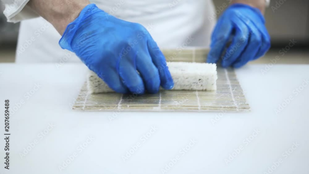 Hands of an unrecognizable skilled Japanese chef in blue gloves forming a sushi with a bamboo mat. Making sushi and traditional Japanese cuisine concept. Locked down real time medium shot Hands of an unrecognizable skilled Japanese chef in blue gloves forming a sushi with a bamboo mat. Making sushi and traditional Japanese cuisine concept. Locked down real time medium shot