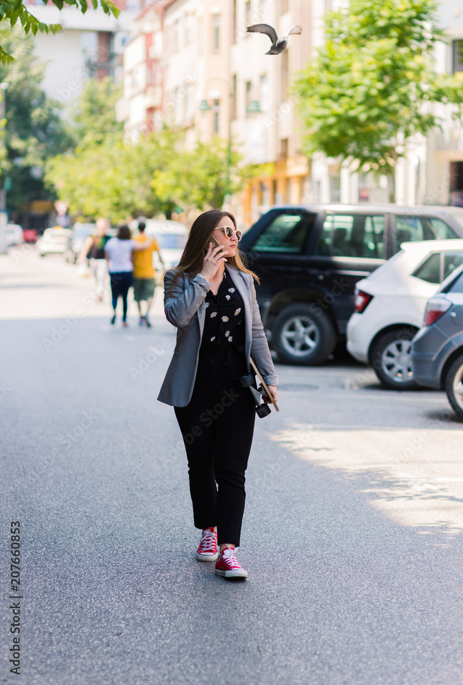 Happy young woman speaking on the phone and holding skate board