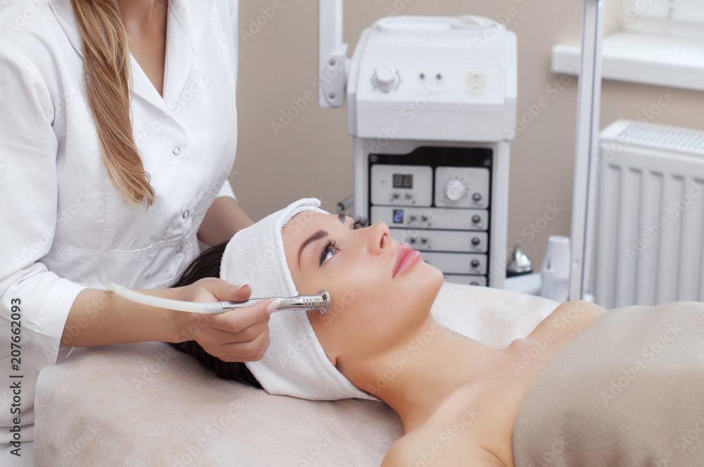 The cosmetologist makes the procedure Microdermabrasion of the facial skin of a beautiful, young woman in a beauty salon.Cosmetology and professional skin care. The cosmetologist makes the procedure Microdermabrasion of the facial skin of a beautiful, young woman in a beauty salon.Cosmetology and professional skin care.