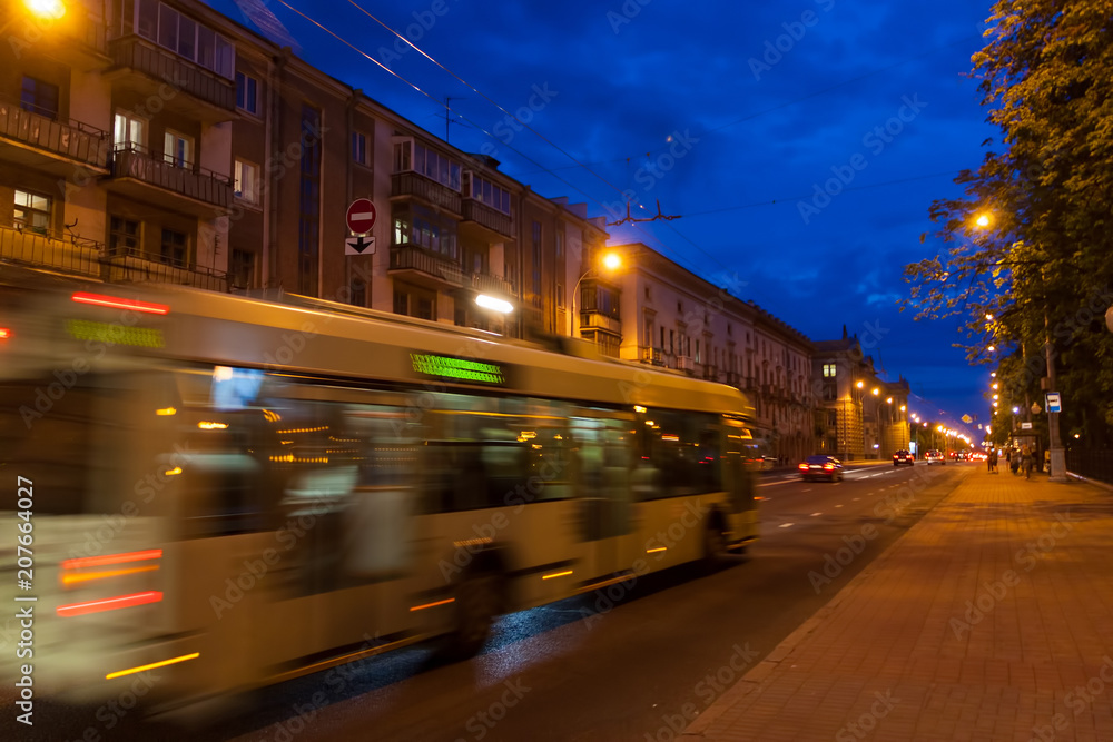 The motion of a blurred trolleybus in the street in the evening.