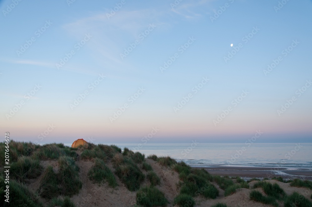 A tent perched on top of a sand dune at dawn