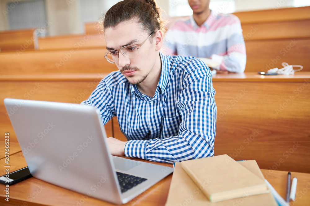 Serious student sitting with laptop at the desk at lesson Serious student sitting with laptop at the desk at lesson