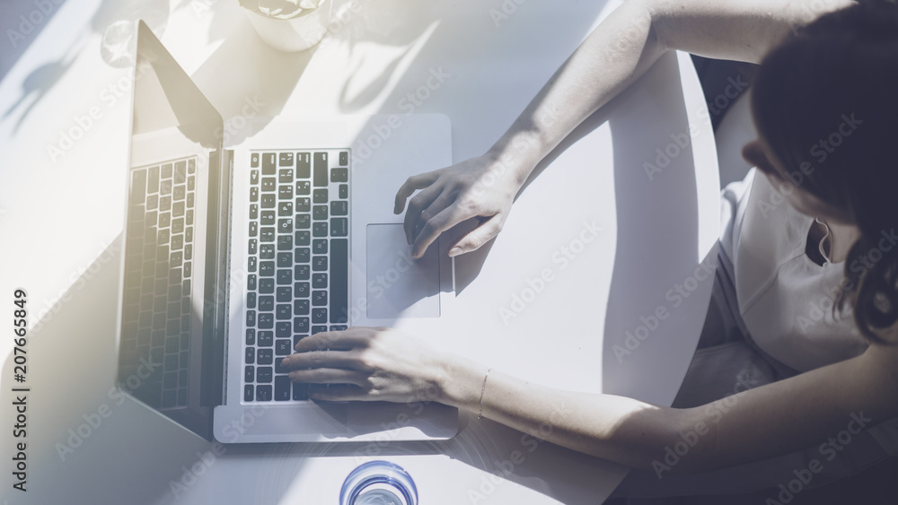 Working moments at home.Young woman typing on laptop computer while sitting at the wooden table in light coloured living room of modern house Working moments at home.Young woman typing on laptop computer while sitting at the wooden table in light coloured living room of modern house