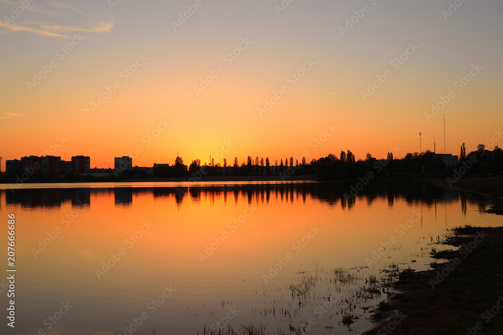 Warm summer sunset over the city lake and beach. Evening cityscape.