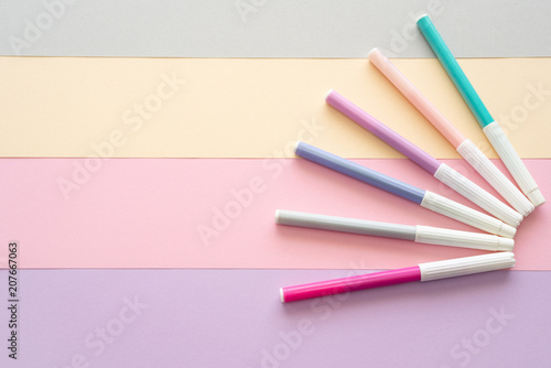 Conjunto de rotuladores de colores pastel sobre un fondo de rayas en tonos pastel con espacio libre para texto a la izquida.
