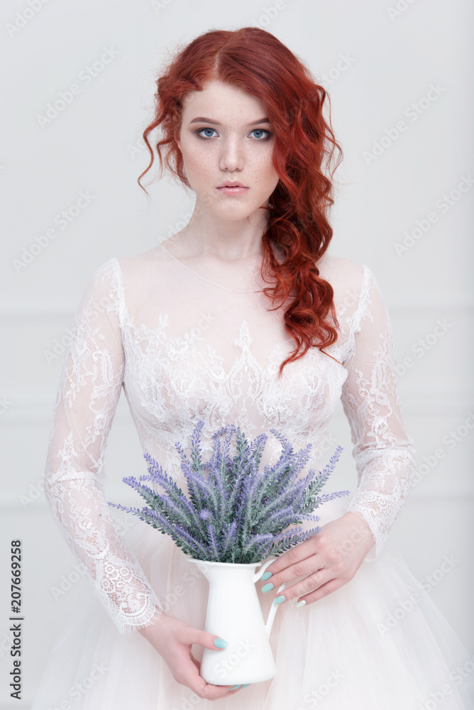 Tender retro portrait of a young beautiful dreamy redhead woman in beautiful white dress with bouquet of lavender.