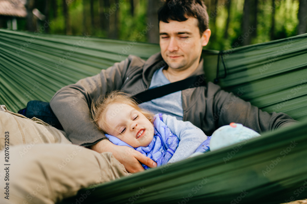 Obraz premium Happy people outdoor. Lifestyle family. Father with his litle artistic funny little child girl resting and playing at nature. Adult male parent with young beautiful daughter lying in hammock in summer