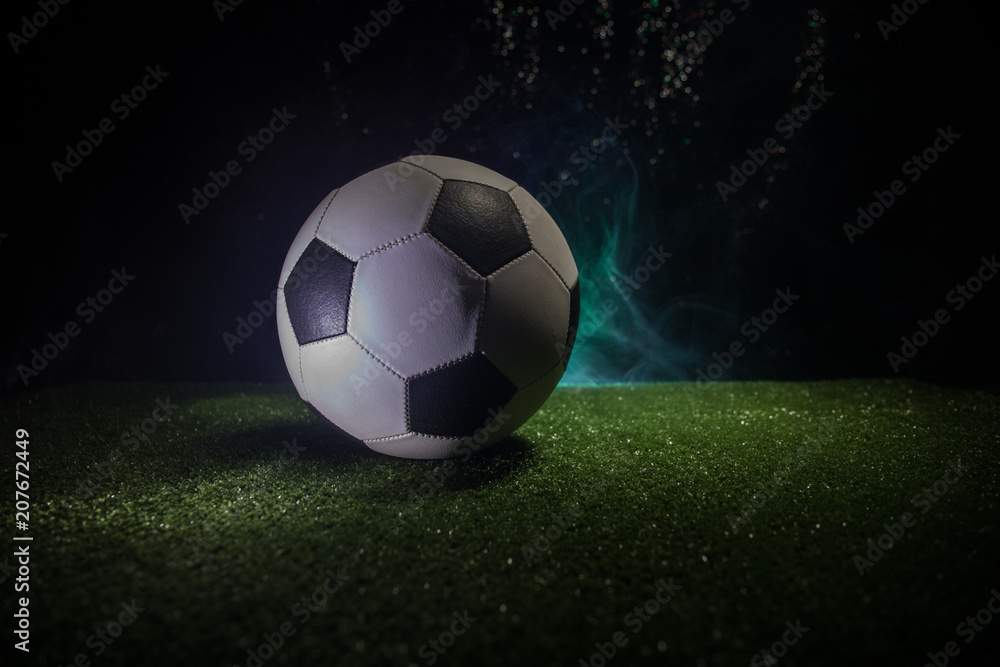 Traditional soccer ball on soccer field. Close up view of soccer ball (football) on green grass with dark toned foggy background.