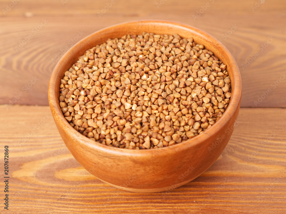 Dry buckwheat in wooden bowl on brown wooden background. Side view. Dry buckwheat in wooden bowl on brown wooden background. Side view.
