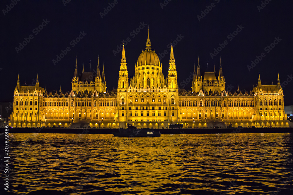 View on Danube river and the illuminated building of Parliament from viewpoint on  a touristic motor ship at night in Budapest, Hungary