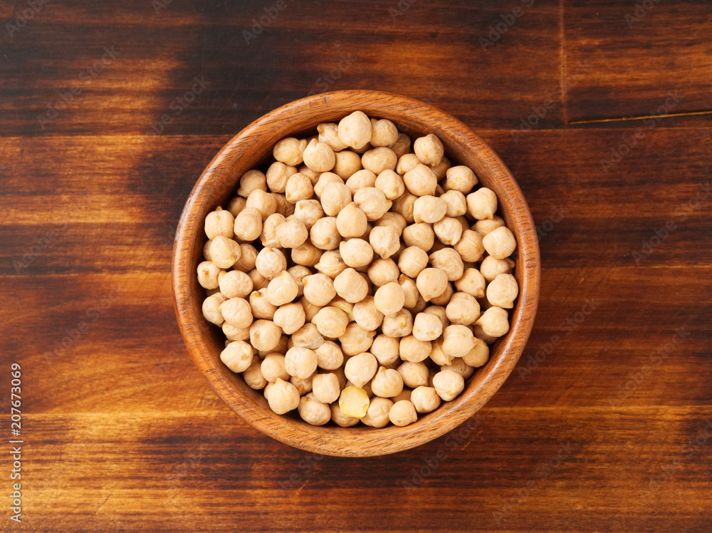 Dry raw chickpeas in wooden bowl on dark brown rustic background, top view Dry raw chickpeas in wooden bowl on dark brown rustic background, top view