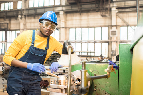 Portrait shot of handsome young lathe operator wearing protective helmet and safety goggles standing at spacious production department of modern plant and looking at camera © Seventyfour