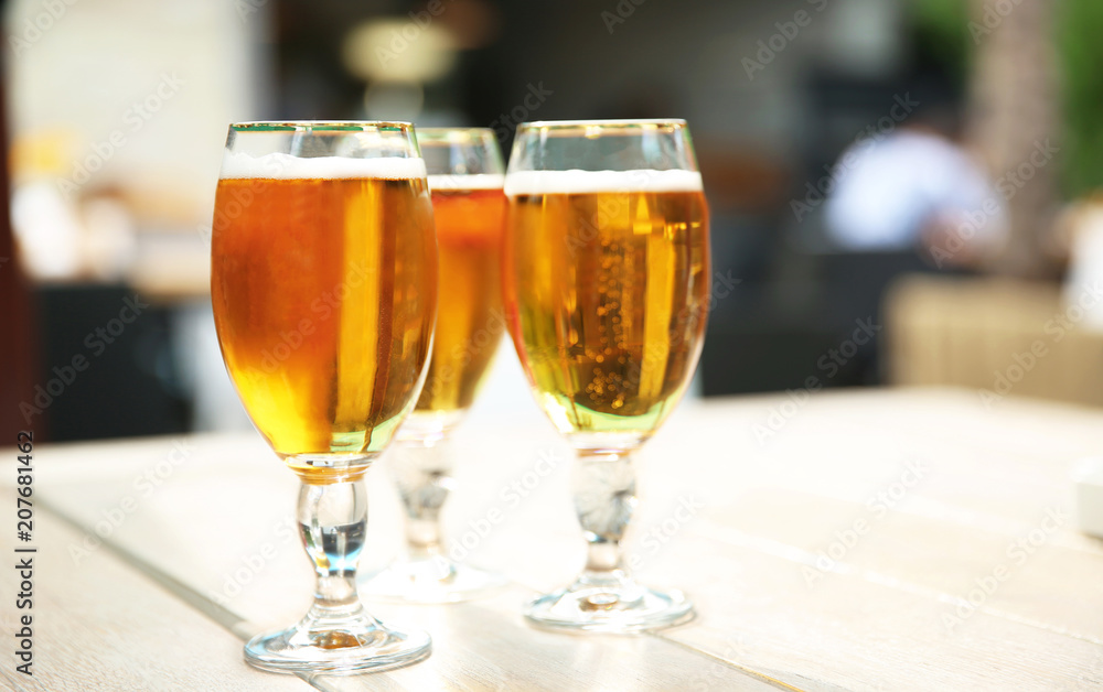 Glasses with cold beer on table against blurred background Glasses with cold beer on table against blurred background