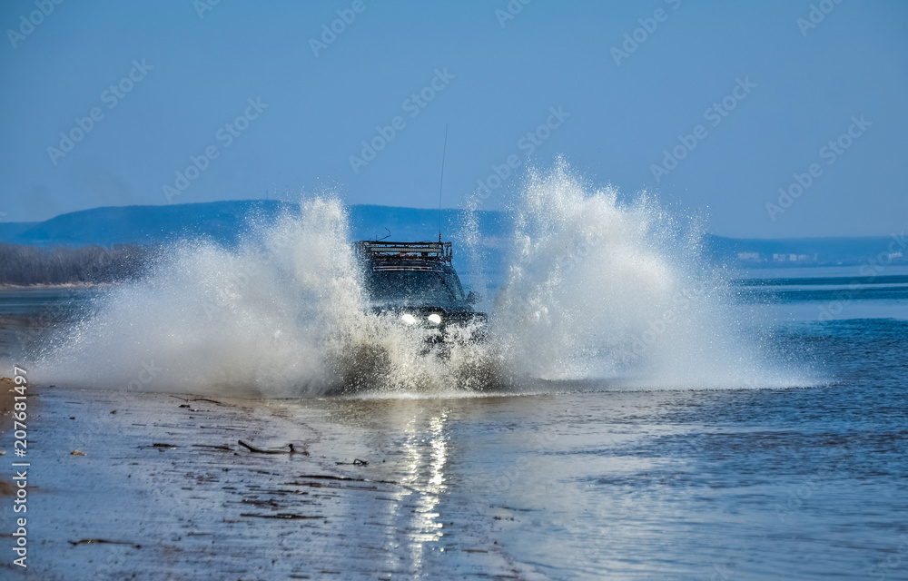 Obraz premium The car goes on water. Splashes from under the wheels. Off-road. Beautiful riding. Car headlight.