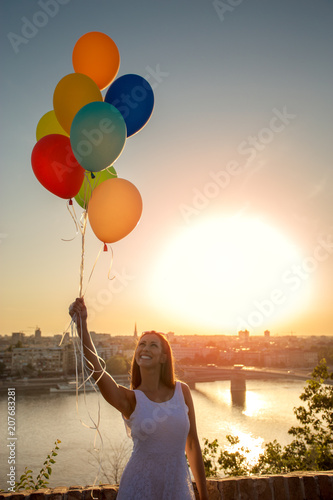 Beautiful young woman holding balloons over a city view while smiling