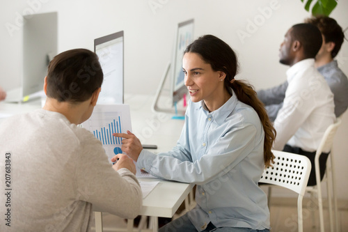 Smiling female worker showing financial graph to male client or colleague, explaining company statistics, talking about sales growth, sharing ideas of business successful strategy. Cooperation concept