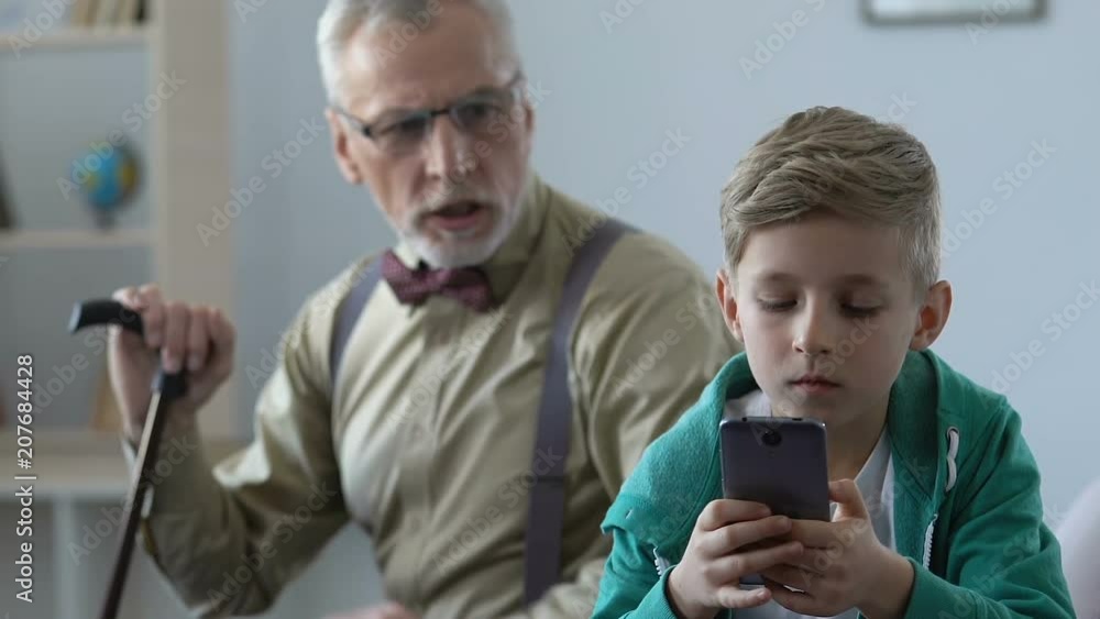 Angry old man scolding grandson playing smartphone game, family misunderstanding Angry old man scolding grandson playing smartphone game, family misunderstanding