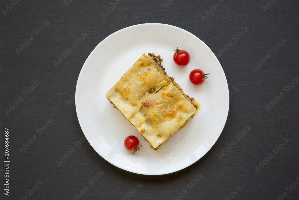 Traditional beef lasagne on a white round plate on black background, top view. Flat lay. From above.