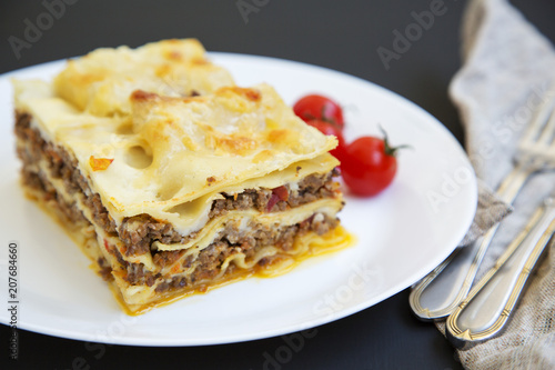 Traditional beef lasagne on a white round plate on black background, side view.