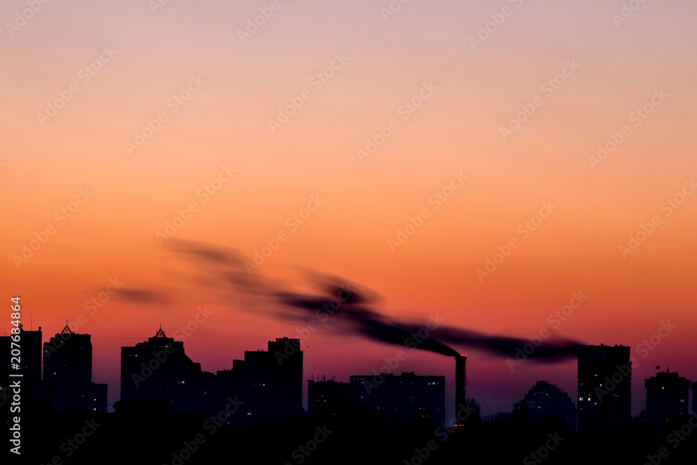 Cityscape with dramatic sky  sunset. Silhouette of buildings and smoking pipes. Urban industrial city.  Environmental pollution