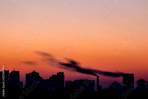 Cityscape with dramatic sky  sunset. Silhouette of buildings and smoking pipes. Urban industrial city.  Environmental pollution