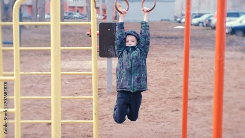 Boy swings on gymnastic rings, jumps and smiles. Playground in the courtyard of the city house. photo