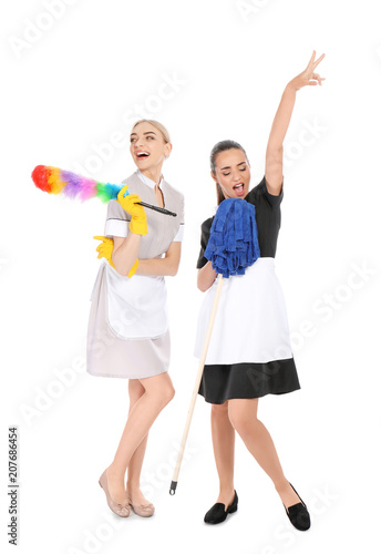 Young chambermaids with dusting brush and mop on white background