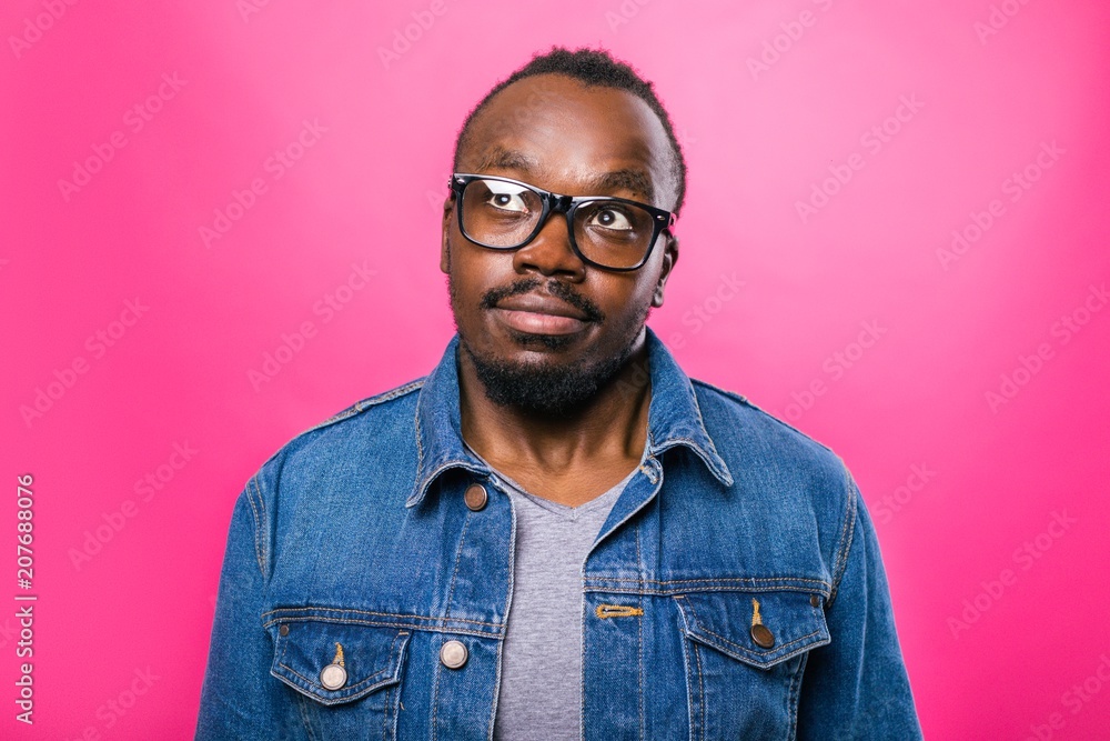 African man in glasses thoughtfully looked up standing in the Studio on a pink background African man in glasses thoughtfully looked up standing in the Studio on a pink background