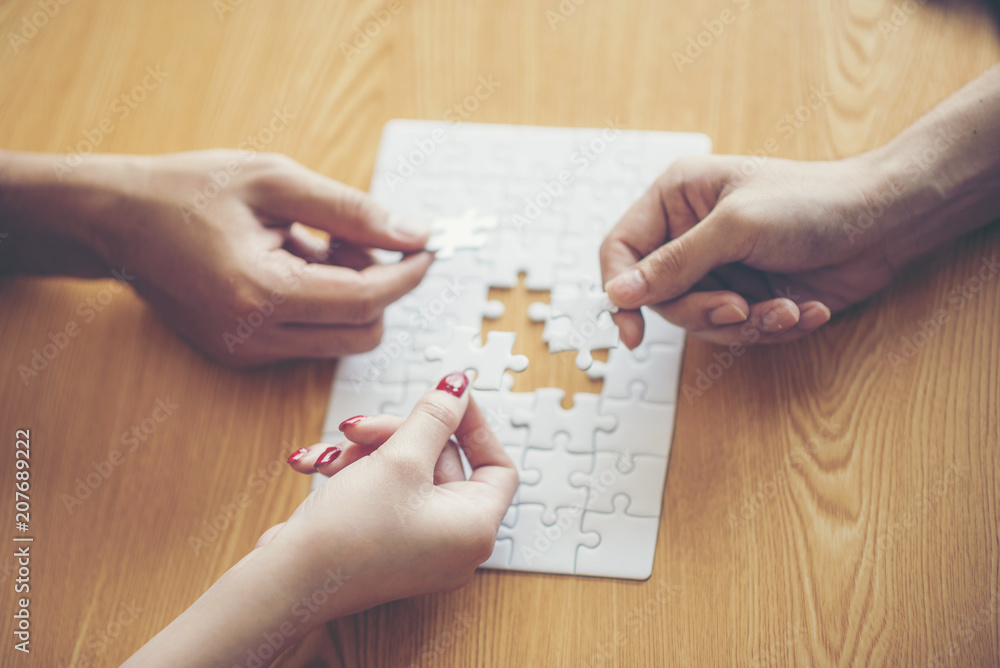 High Angle View Of Businesspeople Hand Solving Jigsaw Puzzle On Wooden Desk High Angle View Of Businesspeople Hand Solving Jigsaw Puzzle On Wooden Desk