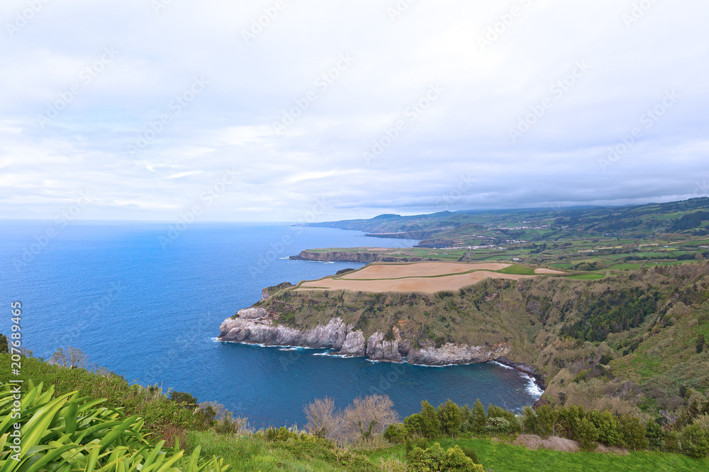 A sweeping view from one of scenic outlooks on Sao Miguel Island of Azores, Portugal. Azorean landscape of the southern coastline of the island in spring. A sweeping view from one of scenic outlooks on Sao Miguel Island of Azores, Portugal. Azorean landscape of the southern coastline of the island in spring.