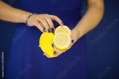 Beautiful woman hands with perfect nail polish holding lemon, yellow fruit on blue, can be used as background